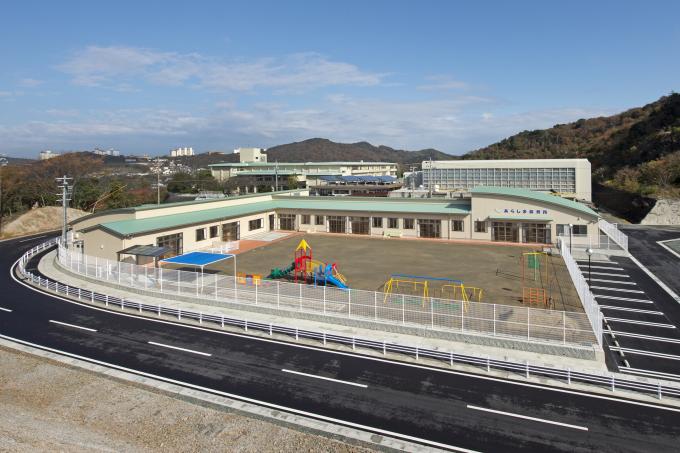 道路沿いにある白い柵で覆われた、緑の屋根で白い園舎の安楽島保育所の写真