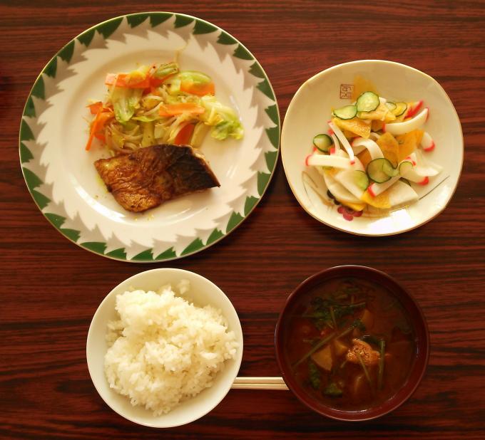 配膳されたさばカレー風味ソテー、柿サラダ、さつまいもと大根葉の味噌汁、白ごはんの写真