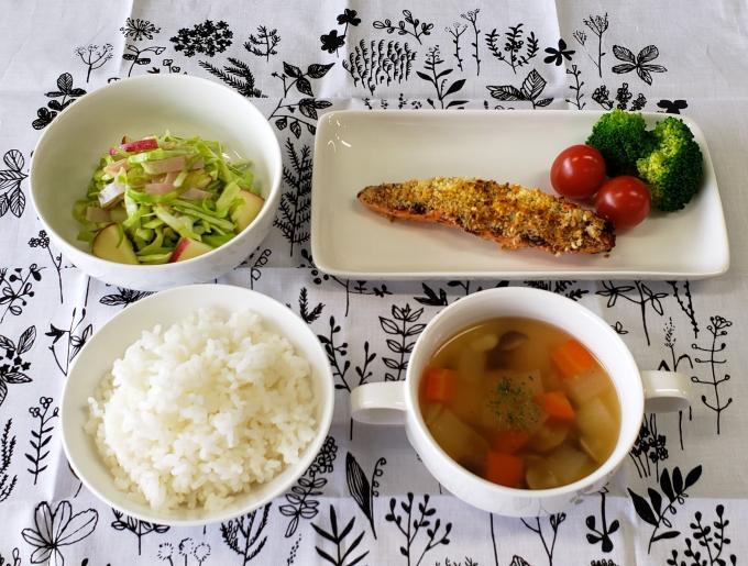 配膳された鮭のパン粉焼き、りんごとキャベツのサラダ、コロコロ野菜のスープ、白ごはんの写真