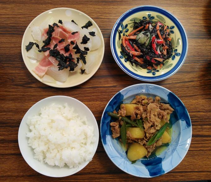 配膳された豚肉と新じゃがいものカレー風味煮、新玉ねぎのレンジ蒸し、ひじきのサラダ、白ごはんの写真