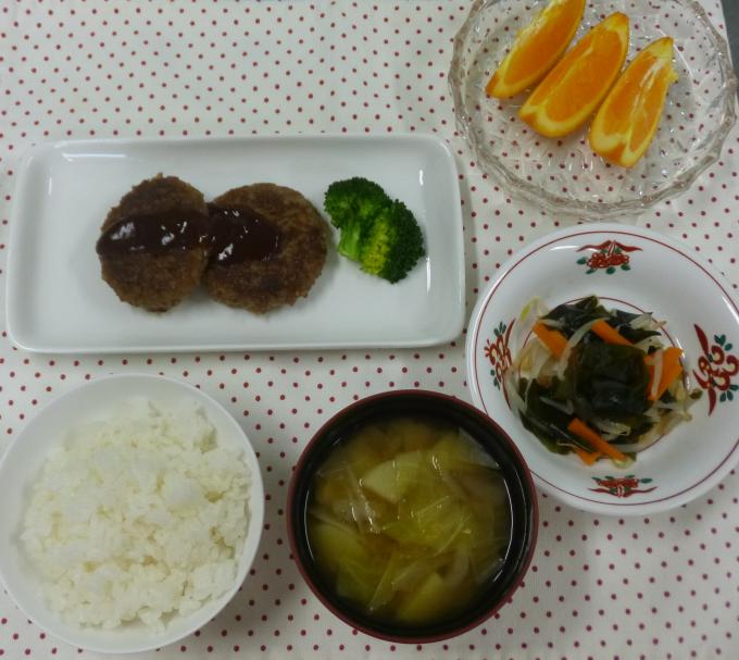 配膳されたきのこハンバーグ、わかめサラダ、キャベツとごぼうの味噌汁、オレンジ、白ごはんの写真