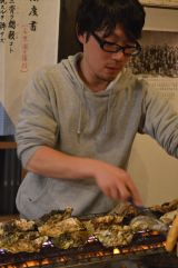 炭火で網の上のかきを焼いている佐藤慎也さんの写真