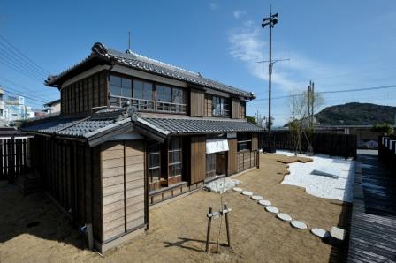 土の上に丸い飛び石が綺麗に並ぶ庭がある、木造2階建ての伊良子清白の写真