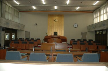 車椅子傍聴席から見える、ベージュの壁と木の机と椅子、名前が用意された議会場の写真
