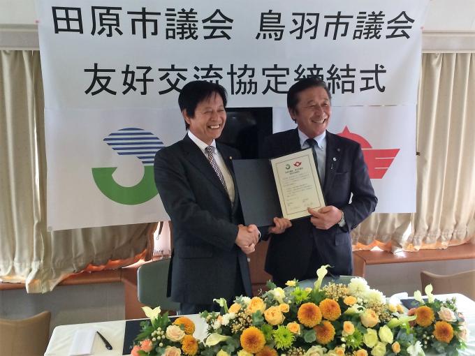 友好交流協定締結式にてにこやかに両市議会議長が協定書を持ちながら握手をしている写真