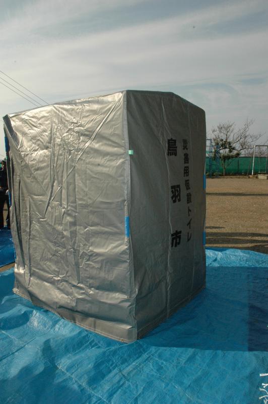 画像:広場に敷かれたブルーシートの上に銀色の四角いテントのような災害用の仮設トイレを設置してある写真