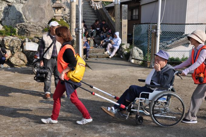 画像:八幡神社の階段の前で、男性が乗っている車椅子を前から引っ張る女性と後ろから押す女性の様子が写った写真