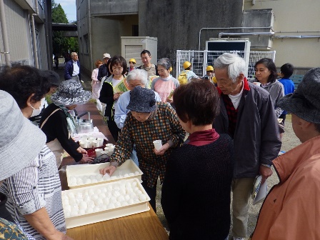 画像:炊き出しの飲み物やおにぎりを、配っている人と選んで受け取っている人と並んでいる人が数人写っている写真
