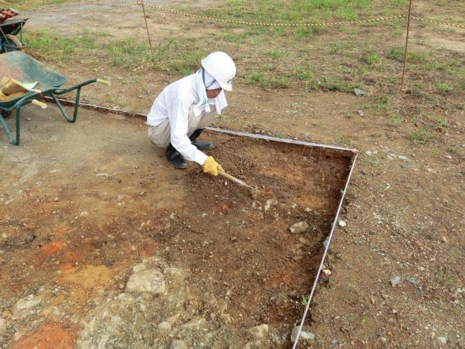白い服を着て白いヘルメットを被り、黄色い手袋をして土を掘っている人の写真