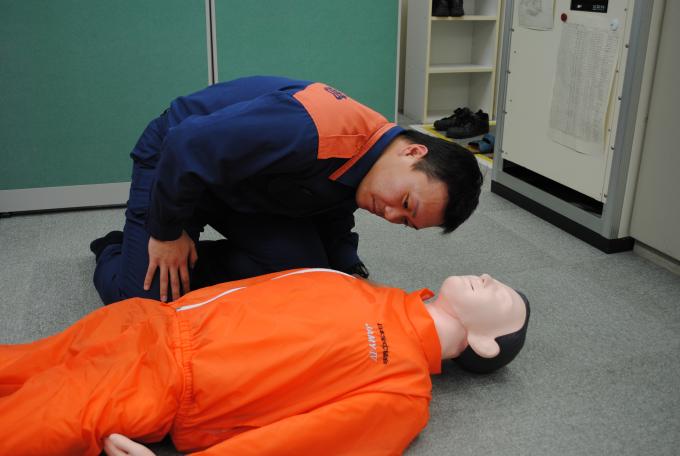 床に横たわる男性の人形の呼吸の様子を観察する男性の写真