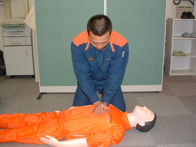 横たわる男性の人形の胸部に、両手をあてる男性の写真