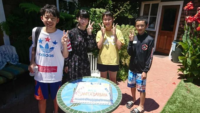 サンタバーバラ市にて、水着姿の4人の中学生が家の前で笑顔でピースをしている写真