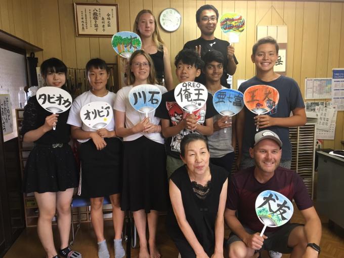 鳥羽市のホームステイ先にて、中学生たちが文字やイラストを描いたうちわを持って、2列に並んで撮った集合写真。