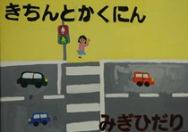 黄色い背景に道路・信号・横断歩道、手を上げて横断歩道を渡ろうとしている女の子、黒い文字で「きちんとかくにんみぎひだり」が描かれたポスター作品