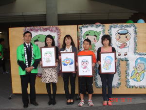 緑色の法被を着た鳥羽市長と受賞された4名が各々自分が描いた作品を持って横一列に並んでいる写真