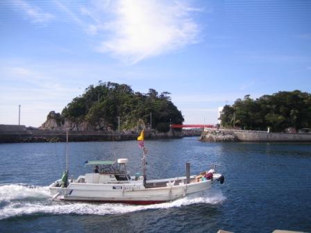 青空の下、手前には船が一艘航海し、遠くに赤い橋が架かった2つの島を臨む、穏やかな伊勢湾の写真