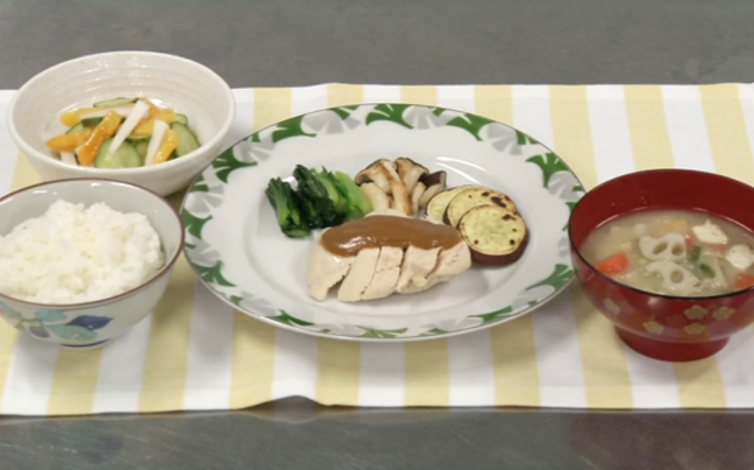 配膳された蒸し鶏のごまソースがけ、柿サラダ、根菜汁、白ごはんの写真