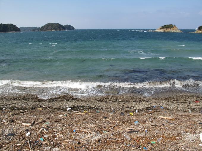 青い海と海岸にたくさんのゴミが漂着している様子の写真
