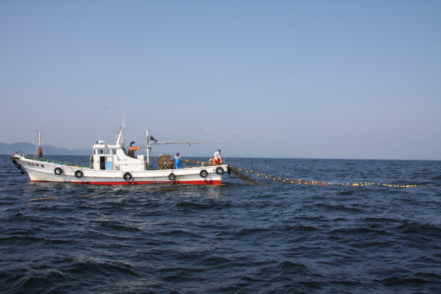 漁船に乗った男性が海面に網を広げている