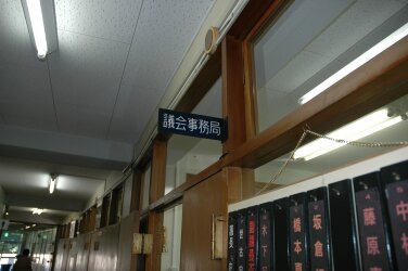 白く、蛍光灯が光る天井と「議会事務局」と書かれた室名札の写真