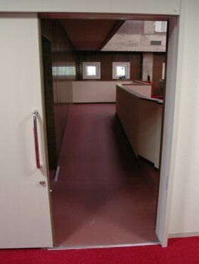 白い引き戸で出来た、薄いピンクの床が見える車椅子用傍聴席入り口の写真
