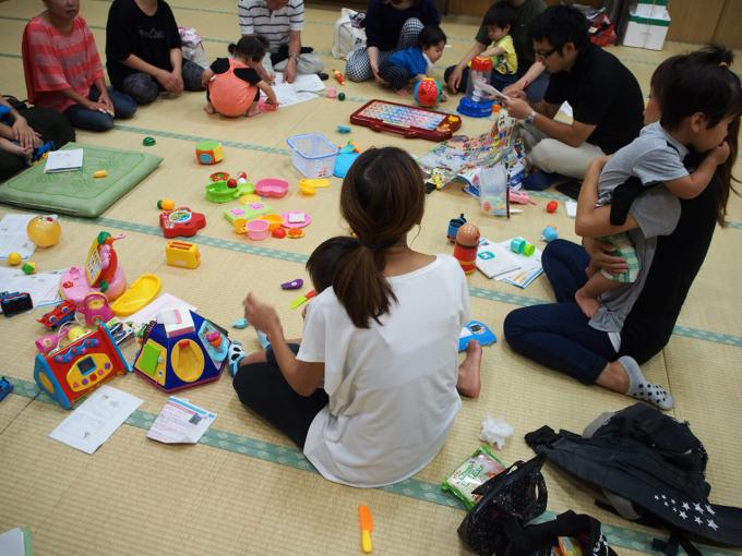 子どもたちや大人たちが一緒になり輪になっておもちゃで遊んでいる写真画像