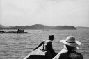 画像：奥には山があり、手前には海と船に乗る2人が写っている白黒の写真