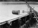 画像：桟橋にいかだの木のくずのようなゴミとドラム缶のようなものが1つ転がっている様子が写っている白黒の写真
