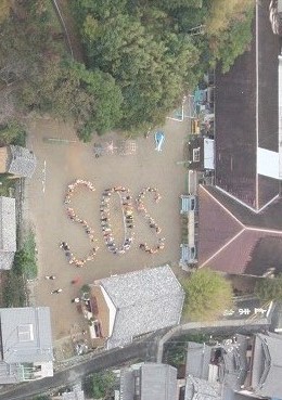 画像：運動場のような広場でSOSの文字を人文字で作り、それを上空から撮影した写真