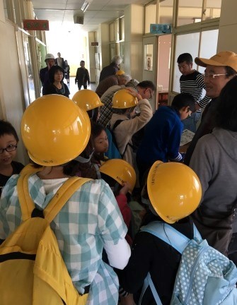 画像：学校内の廊下で黄色いヘルメットを被っている人や訓練に参加している人が大勢写っている写真