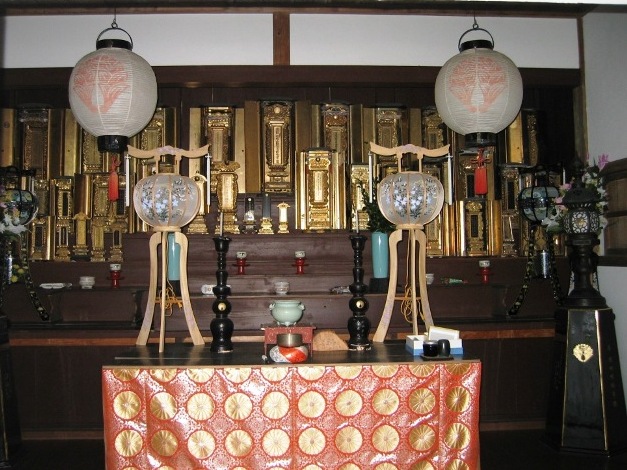 金色の霊廟、複数の位牌、二つの白い提灯、二つの盆提灯、二本の蝋燭立て、薄緑色の線香立て、金色のお鈴が置かれている稲垣氏歴代の廟所の写真画像