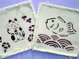 紫色のインクで1枚は魚、もう1枚は招き猫の絵が描かれた真四角の白い生地の写真
