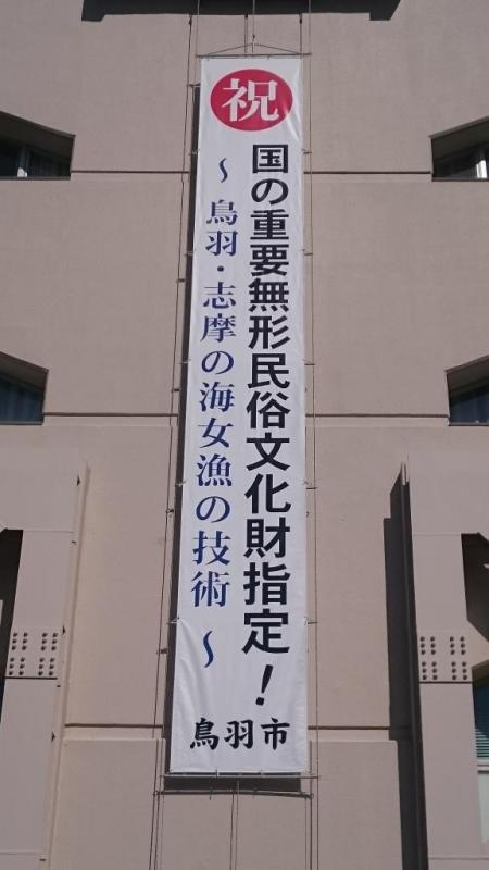 赤丸に白地で祝、黒字で国の重要無形民俗文化財指定！青字で鳥羽・志摩の海女漁の技術と記載された、建物の壁にかかっている大きな垂幕の写真