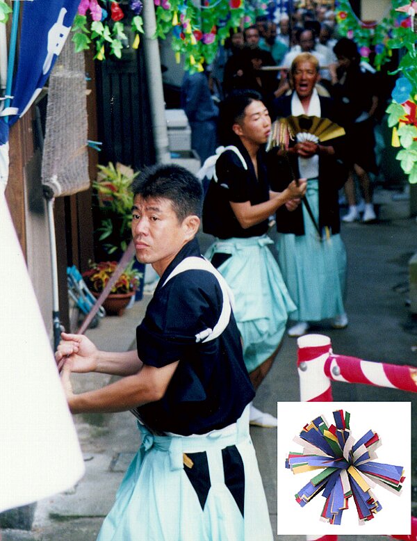 和装の男性たちが五色の細い紙をつけた棒を回して神社まで練りこんでいる坂手の棒練りの写真画像