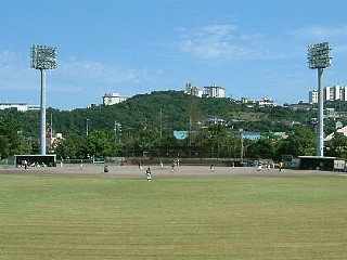 山を背に一面に広がる野球場で、ユニホームを着た選手達が試合をしている写真