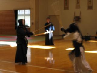 武道館の中で、剣道の試合をする二人と見守る男性の写真