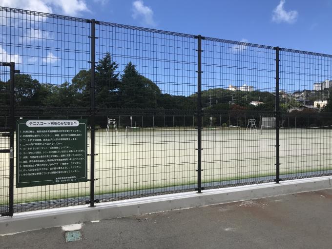「テニスコートをご利用のみなさまへ」という緑の看板と、フェンス越しに見えるテニスコートの写真
