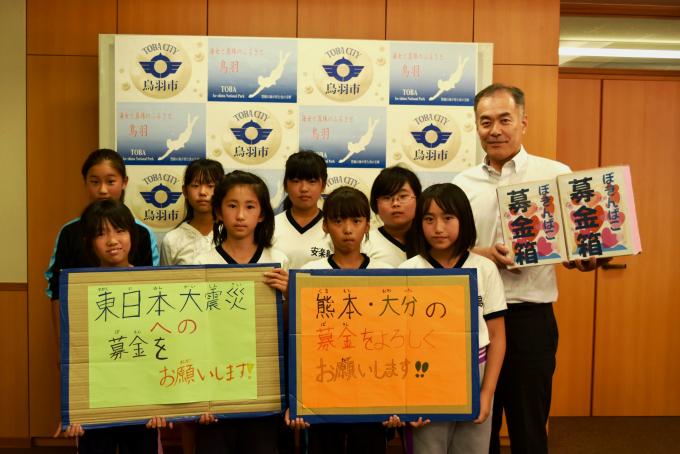 画像：「東日本大震災への募金をお願いします！」と書かれたボードと「熊本・大分の募金をよろしくお願いします！」と書かれたボードを持っている小学生くらいの子どもたち8人と、募金箱と書かれた箱を持っている中村市長が写った記念写真