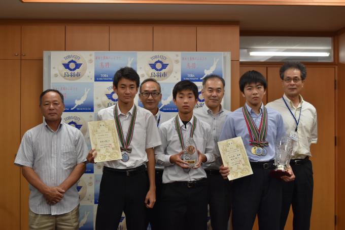 画像：全国中学生フェンシング選手権大会に出場した小崎一磨さん、木場悠斗さん、小久保真旺さんが賞状やトロフィを持ちながら、中村市長と男性3名と並んで写っている記念写真