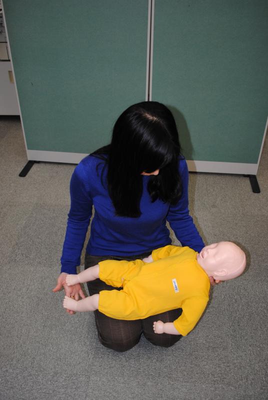 乳児の人形を膝に乗せ、足の裏を叩く女性の写真