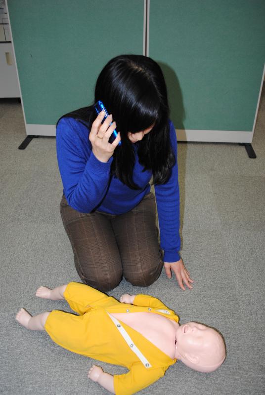 床に横たわる乳児を見つめながら、電話をする女性の写真