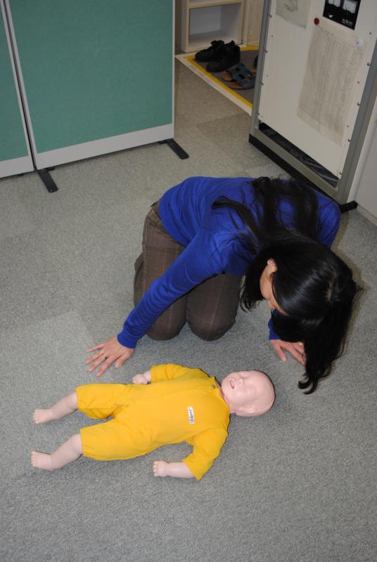 床に横たわる乳児の腹部や胸部を上から観察する女性の写真