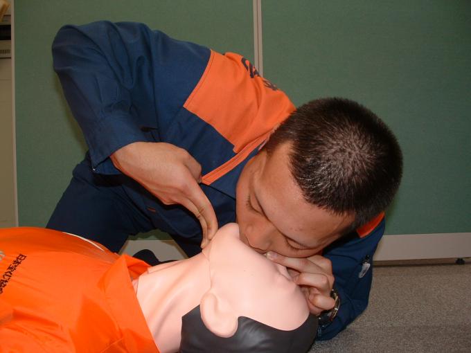 床に横たわる人形の顎を持ち上げ、口から息を吹き込む男性の写真