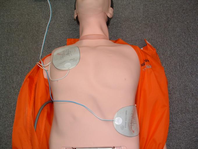 床に横たわる男性の人形の鎖骨の下と左腹部の脇に電極パッドが貼ってある写真