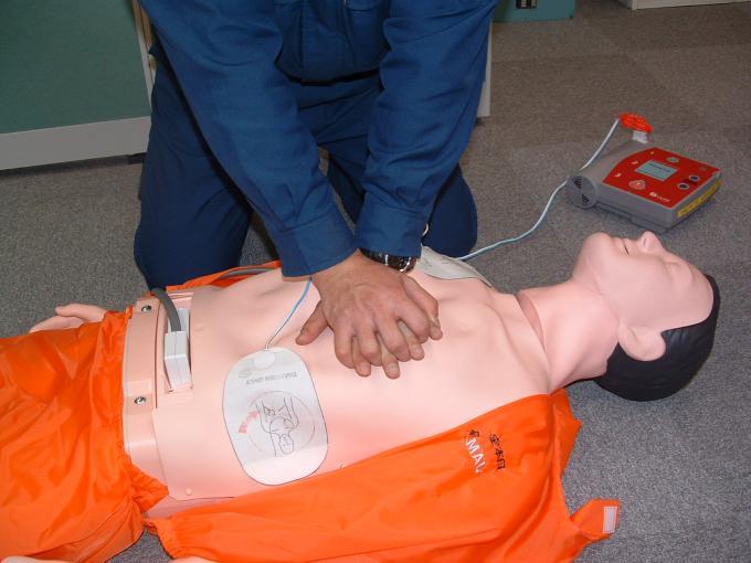AEDの電極パッドをつけた男性の人形の胸に両手をあて、胸骨を圧迫する男性の写真
