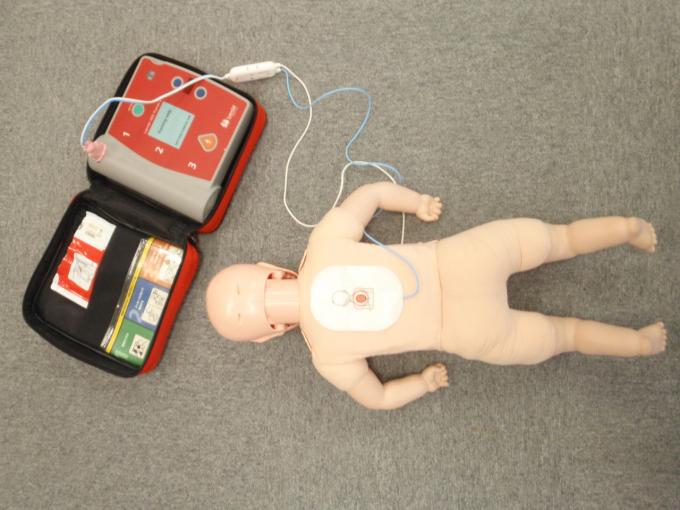 うつ伏せに寝ている小児用の人形の背中に、AEDの電極パッドを貼り付けた写真