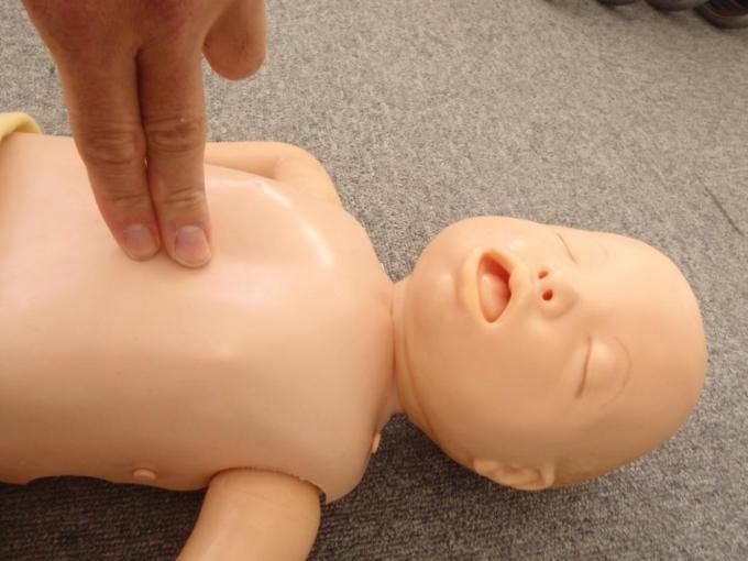 床に横たわる乳児の胸部に人差し指、中指の2本の指をあてている写真