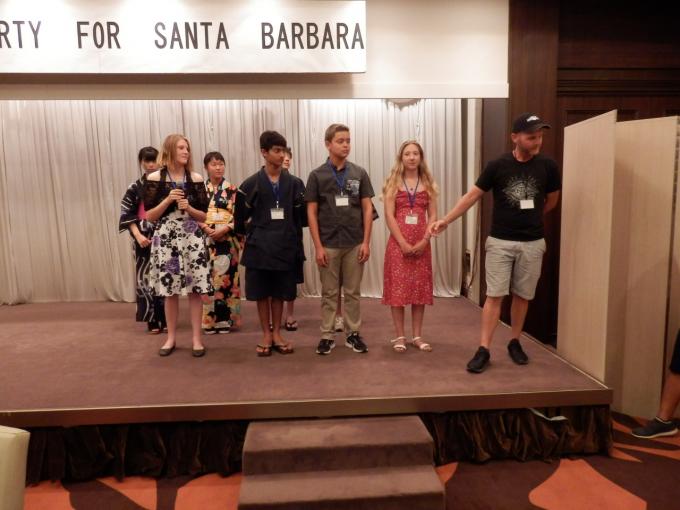 ホテルの宴会場のステージ上に並び、マイクを持って話をするサンタバーバラ市中学生たちの写真。