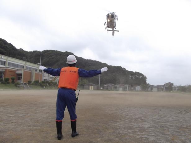 グラウンドに着陸しようとするヘリコプターと、それを誘導する人の写真。